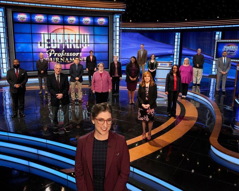 host and contestants standing on the Jeopardy television set